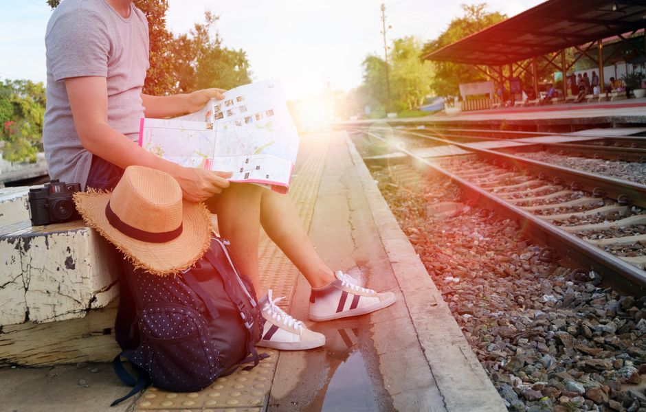 Person sitting at train station platform reading map, embracing travel adventure.